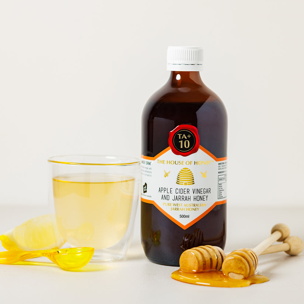 Bottle of apple cider vinegar and jarrah honey with a glass of liquid and honey dipper on a white background