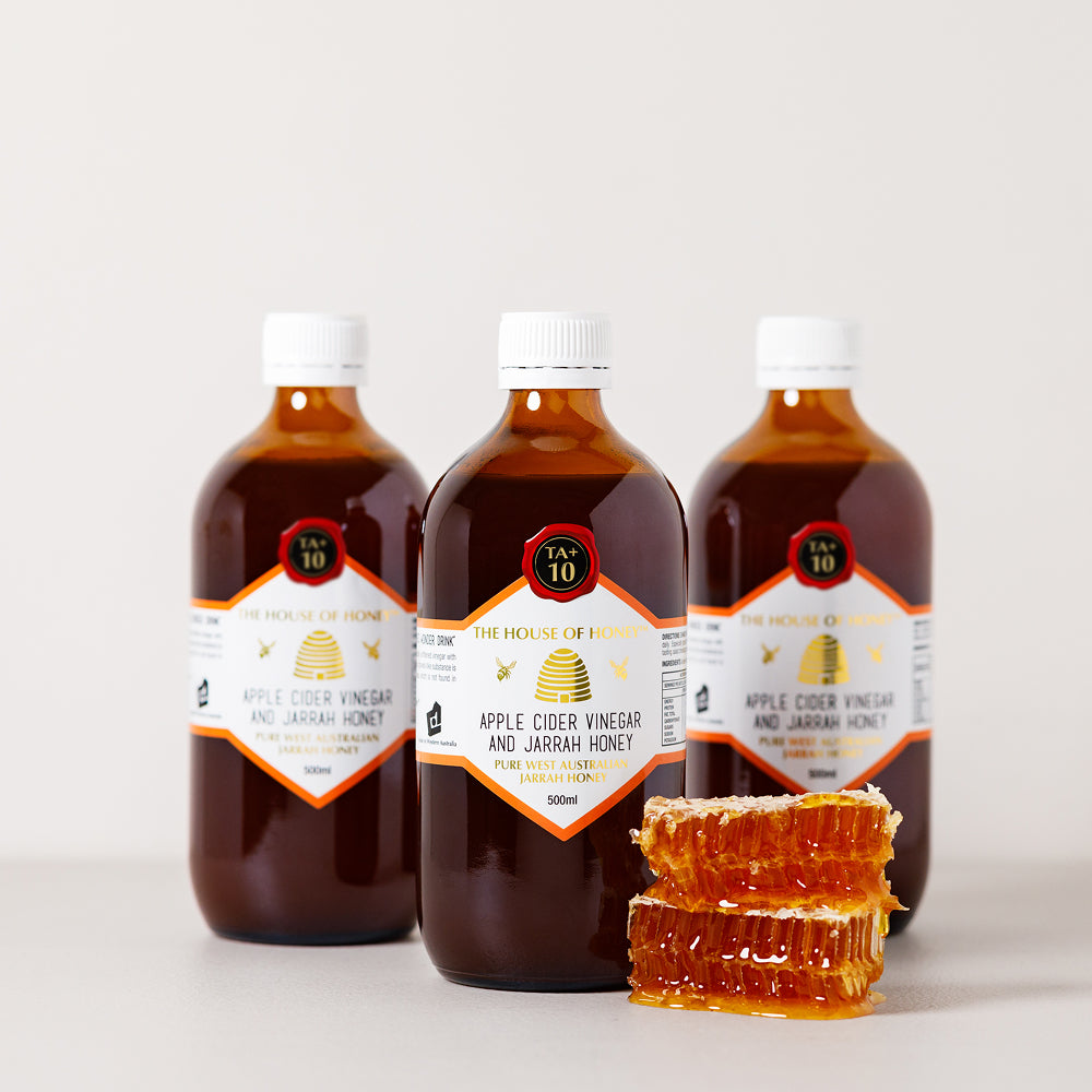 Three bottles of Apple Cider Vinegar and Jarrah Honey with a stack of honeycomb on a light background