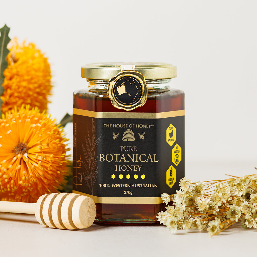 Jar of pure botanical honey with flowers and a honey dipper on a white background