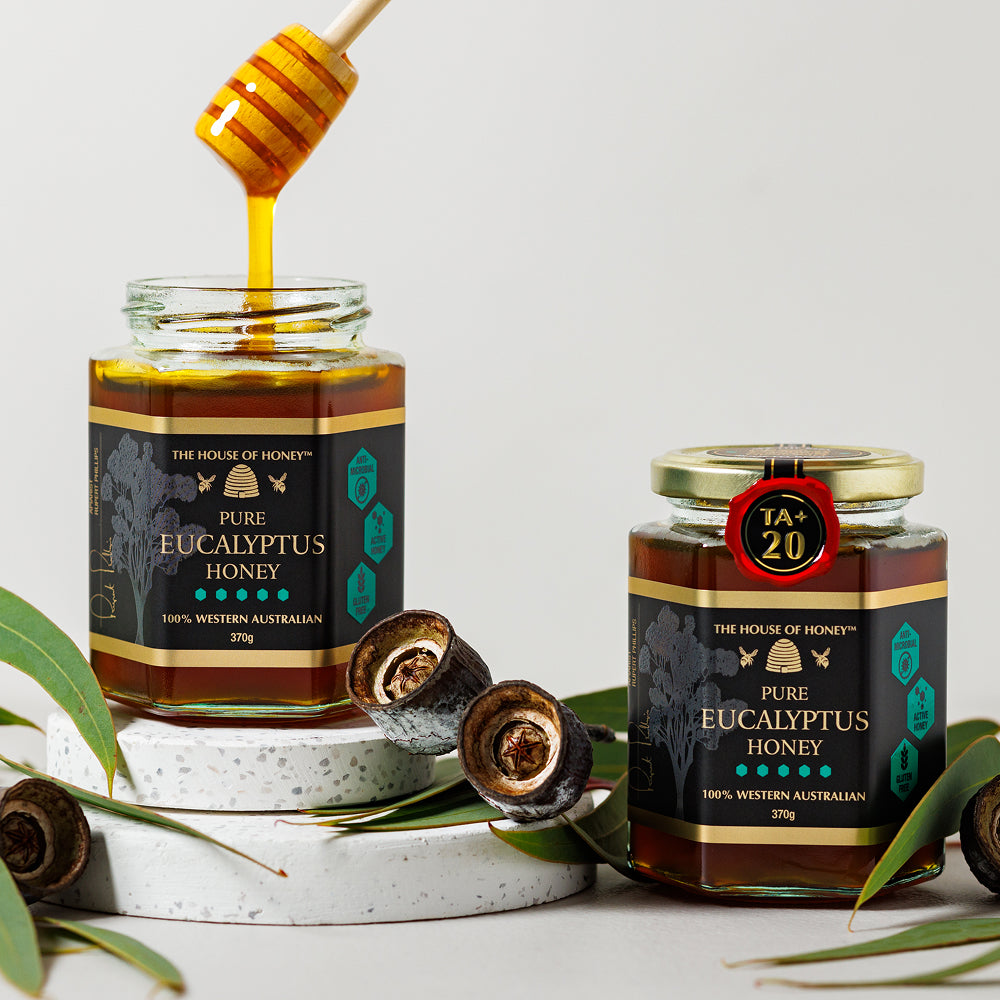 Two jars of pure eucalyptus honey with a honey dipper and eucalyptus leaves on a light background.