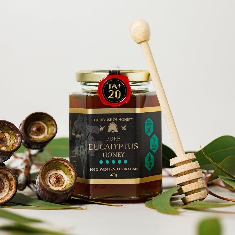 Jar of pure eucalyptus honey with a wooden dipper on a light background