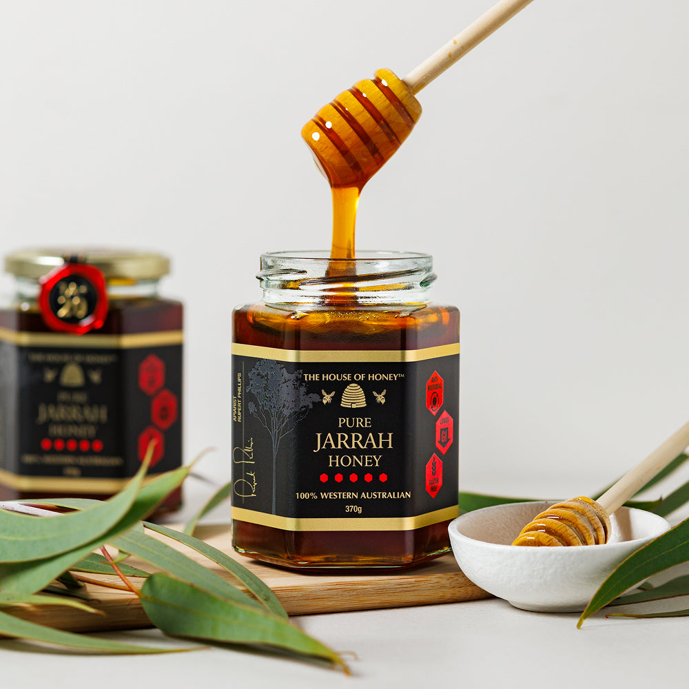 Jar of Pure Jarrah Honey with a honey dipper and jar in the background on a light background