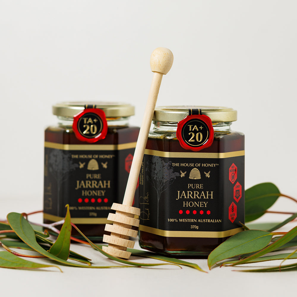 Two jars of Pure Jarrah Honey with a wooden honey dipper on a white background.
